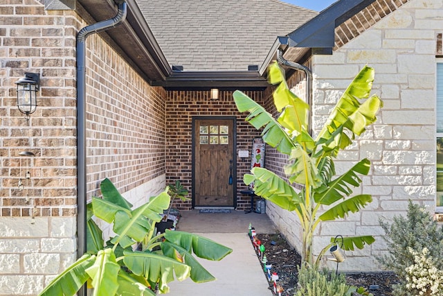 doorway to property featuring brick siding and roof with shingles