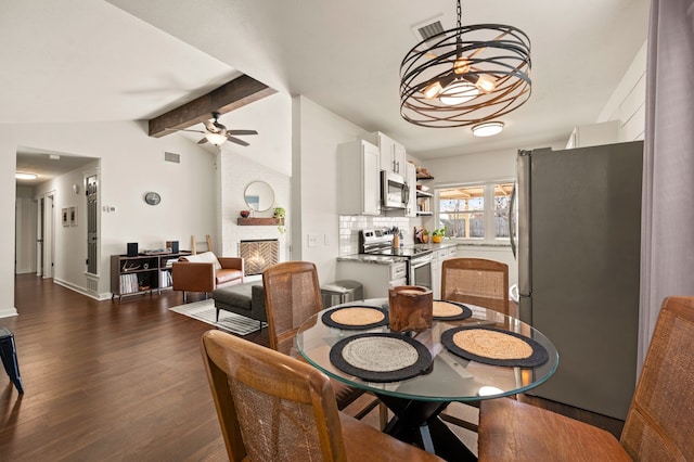 dining room featuring dark wood-type flooring, a large fireplace, visible vents, and lofted ceiling with beams