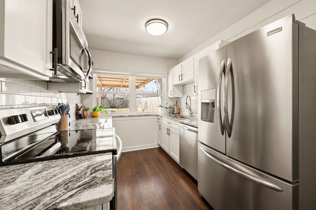 kitchen with appliances with stainless steel finishes, a sink, light stone counters, and white cabinetry