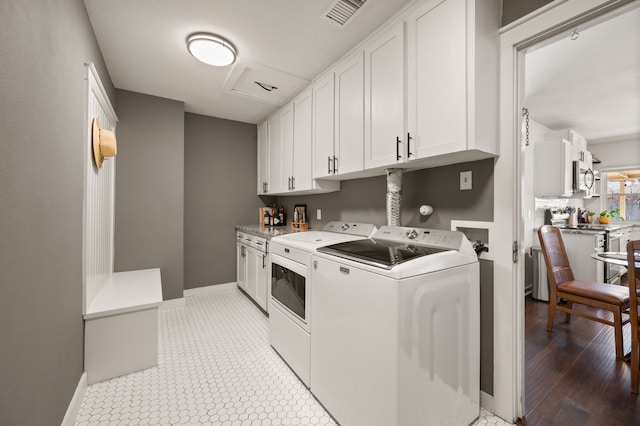 clothes washing area with washer and dryer, visible vents, cabinet space, and baseboards