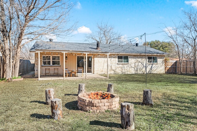 back of property with a fenced backyard, a fire pit, brick siding, a lawn, and a patio area