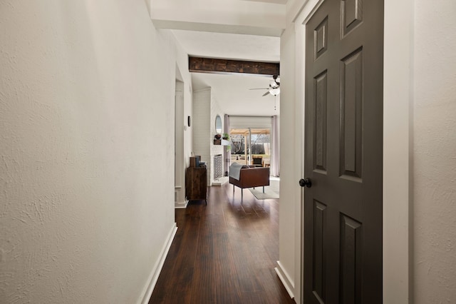 hallway featuring baseboards, dark wood finished floors, beamed ceiling, and a textured wall