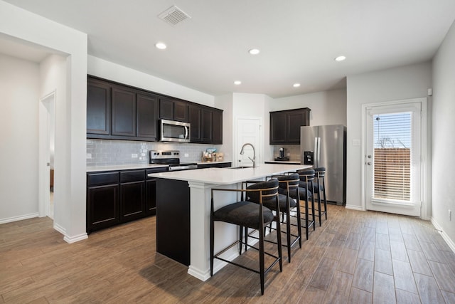 kitchen with visible vents, appliances with stainless steel finishes, light wood-style floors, a kitchen bar, and a sink