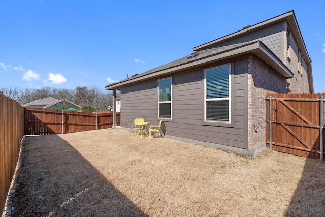 rear view of property with brick siding, a fenced backyard, and a gate