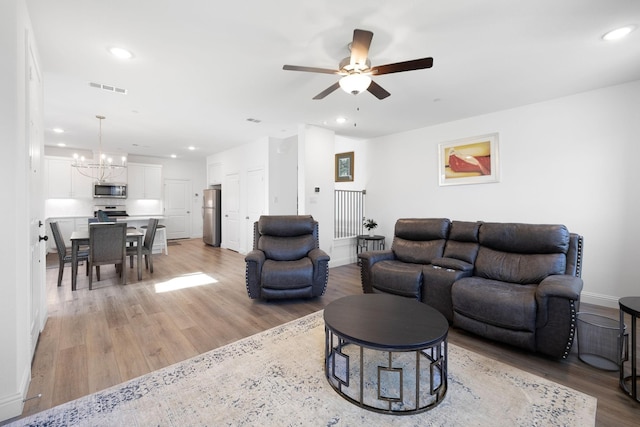 living area with recessed lighting, visible vents, light wood-style floors, baseboards, and ceiling fan with notable chandelier