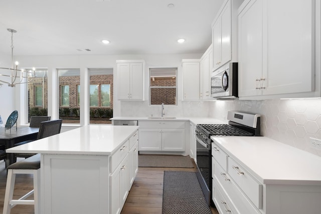 kitchen with light countertops, appliances with stainless steel finishes, a sink, a kitchen island, and a kitchen breakfast bar