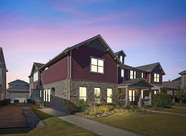 view of front of home featuring board and batten siding, stone siding, covered porch, and a lawn