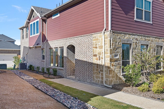 view of side of home with stone siding, central AC unit, and brick siding