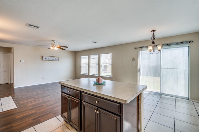 kitchen featuring light tile patterned floors, light countertops, visible vents, a kitchen island, and dark brown cabinetry