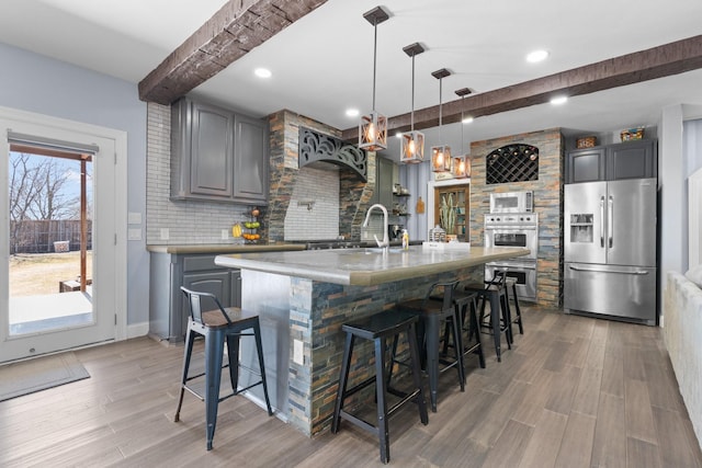 kitchen with stainless steel appliances, beamed ceiling, light wood-type flooring, and a sink