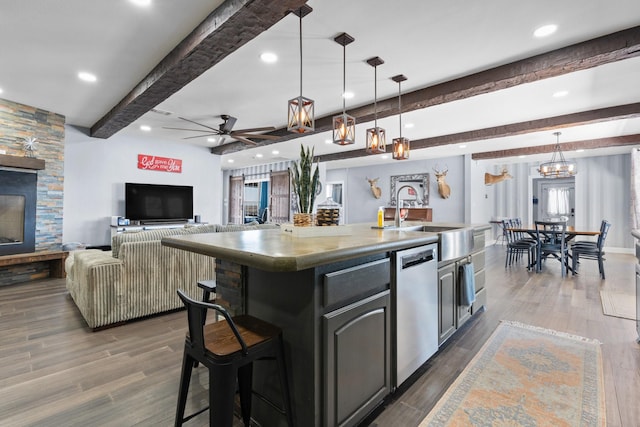 kitchen featuring an island with sink, dark wood-style flooring, beamed ceiling, a sink, and stainless steel dishwasher