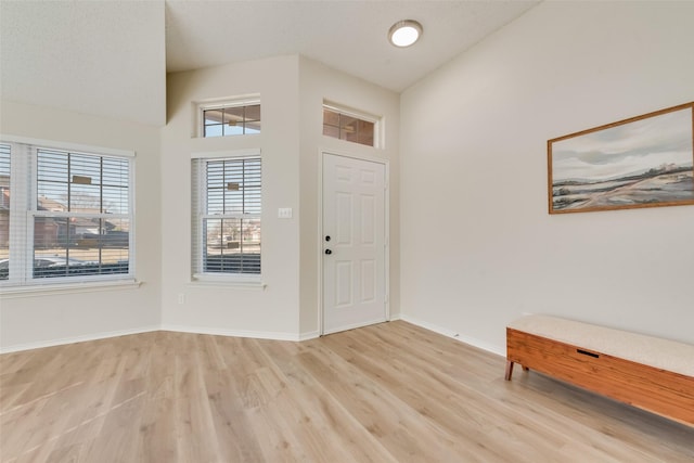 entrance foyer featuring high vaulted ceiling, light wood-style flooring, and baseboards