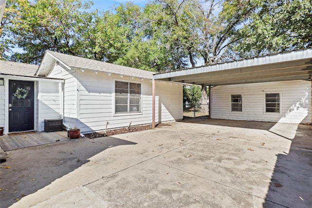 rear view of property featuring a carport, concrete driveway, and a shingled roof