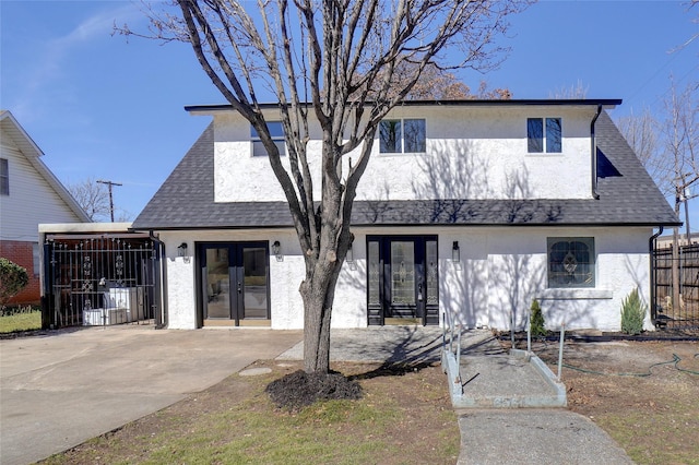 view of front facade featuring french doors, roof with shingles, fence, and stucco siding