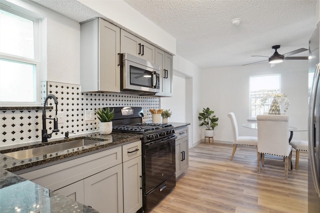 kitchen with stainless steel microwave, light wood-style floors, black gas stove, a sink, and dark stone counters