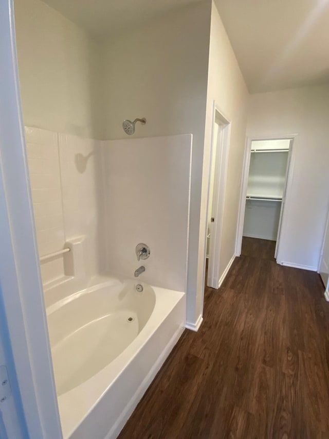 full bath featuring  shower combination, a walk in closet, baseboards, and wood finished floors