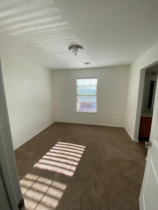 unfurnished room featuring dark colored carpet, visible vents, and baseboards