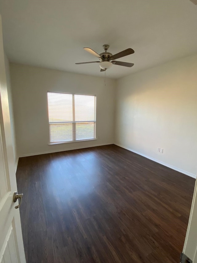 empty room with a ceiling fan, dark wood finished floors, and baseboards