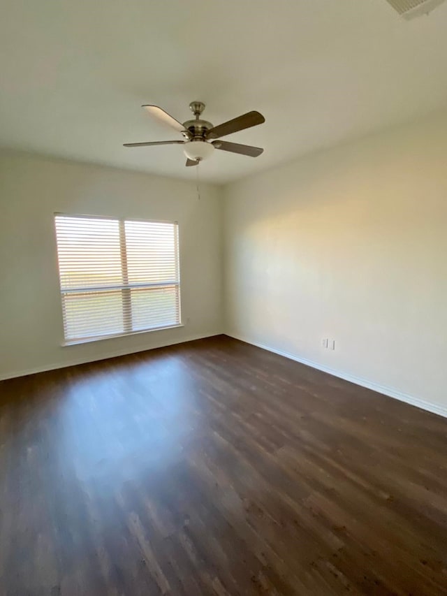 unfurnished room with dark wood-type flooring, a ceiling fan, and baseboards