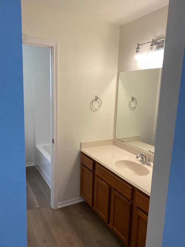 full bathroom with a bathing tub, baseboards, wood finished floors, and vanity