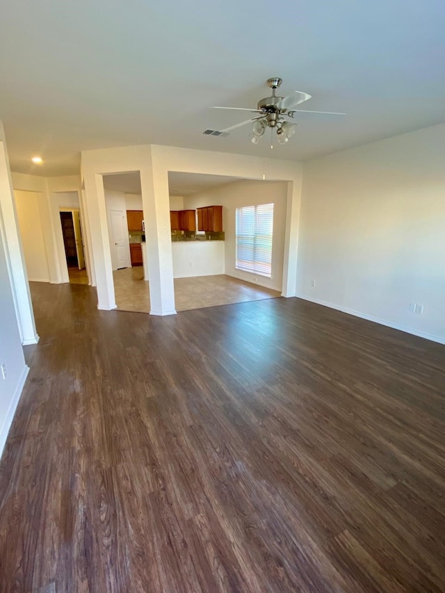 unfurnished living room with dark wood-style floors, ceiling fan, visible vents, and baseboards