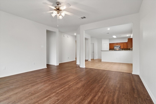unfurnished living room featuring baseboards, dark wood-style floors, visible vents, and ceiling fan