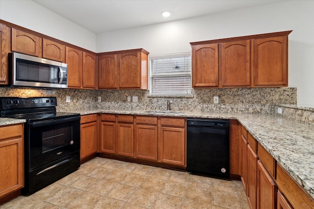 kitchen featuring light stone counters, brown cabinetry, a sink, decorative backsplash, and black appliances