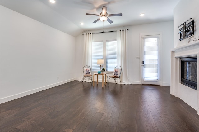 sitting room with vaulted ceiling, dark wood-type flooring, a tiled fireplace, and baseboards