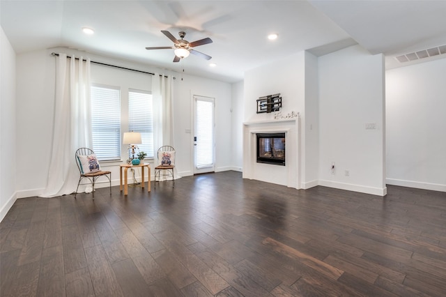 living area featuring baseboards, visible vents, a glass covered fireplace, dark wood-type flooring, and vaulted ceiling