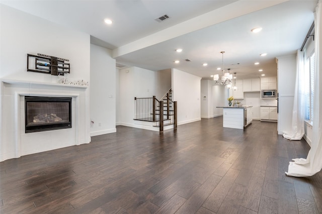 unfurnished living room with dark wood-style flooring, recessed lighting, visible vents, a tiled fireplace, and stairs