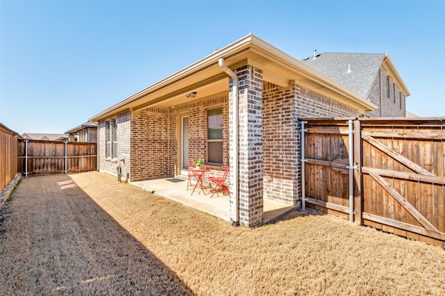 view of side of property featuring brick siding, a patio area, fence, and a gate