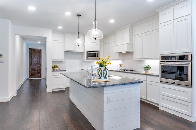 kitchen featuring appliances with stainless steel finishes, dark stone countertops, dark wood finished floors, and tasteful backsplash