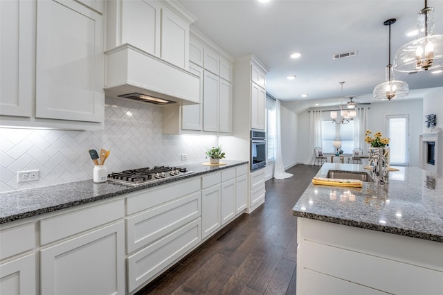 kitchen with stainless steel appliances, a sink, white cabinetry, backsplash, and dark stone countertops