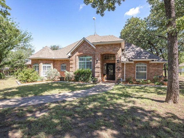 view of front of house featuring a shingled roof, a front yard, and brick siding