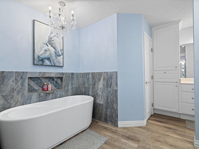 bathroom featuring a textured ceiling, a freestanding tub, wood finished floors, vanity, and tile walls