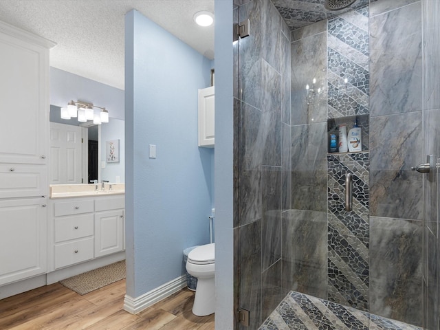 bathroom featuring toilet, wood finished floors, a textured ceiling, vanity, and a shower stall