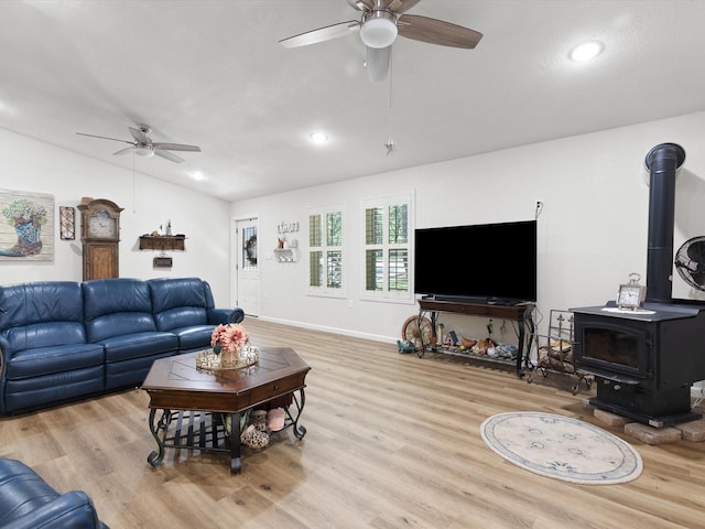 living area featuring lofted ceiling, wood finished floors, a wood stove, and a ceiling fan