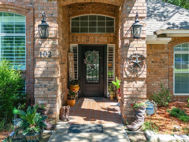 entrance to property featuring a shingled roof and brick siding