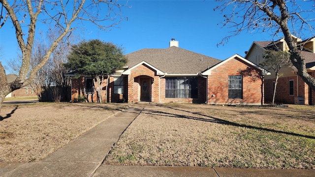 ranch-style house featuring a shingled roof, brick siding, a chimney, and a front lawn