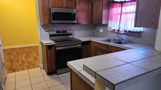 kitchen featuring light tile patterned floors, decorative backsplash, appliances with stainless steel finishes, a sink, and a peninsula