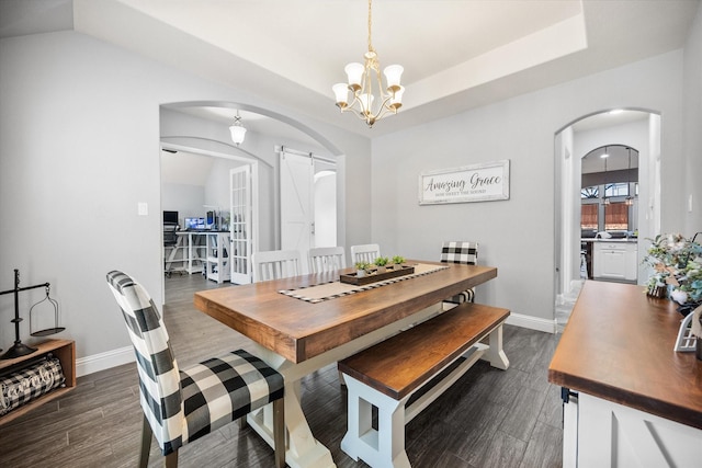 dining room featuring arched walkways, a tray ceiling, a barn door, and dark wood-style flooring