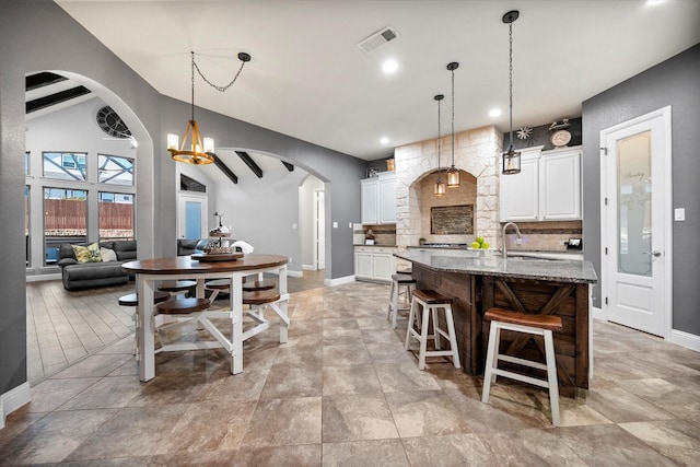 kitchen with arched walkways, a sink, visible vents, white cabinets, and decorative backsplash