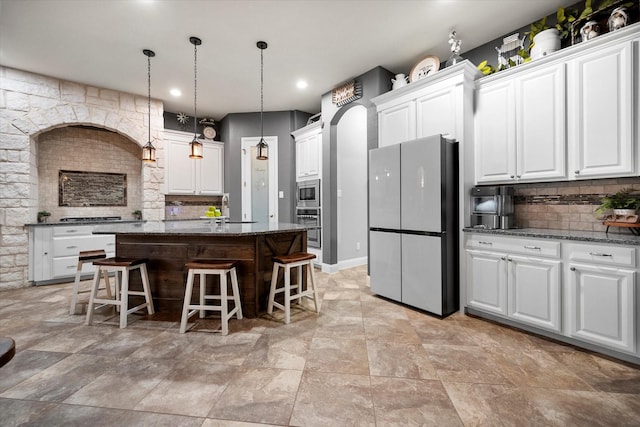 kitchen with appliances with stainless steel finishes, dark stone countertops, a kitchen bar, white cabinetry, and backsplash