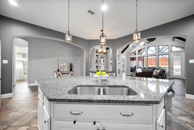 kitchen with arched walkways, a kitchen island with sink, visible vents, open floor plan, and vaulted ceiling