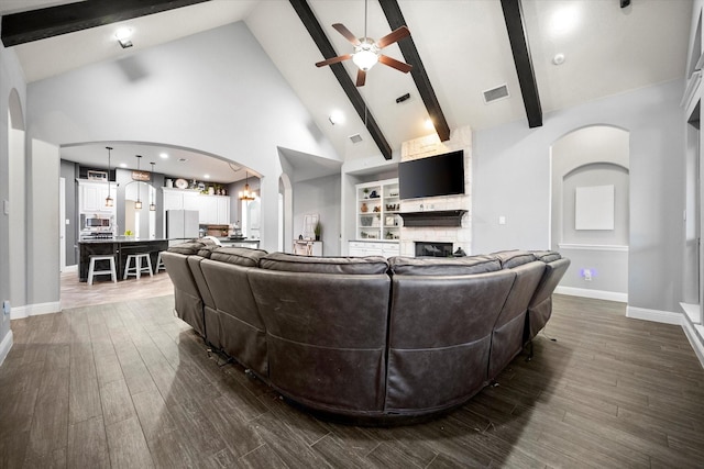 living area featuring arched walkways, visible vents, dark wood-type flooring, ceiling fan, and a stone fireplace