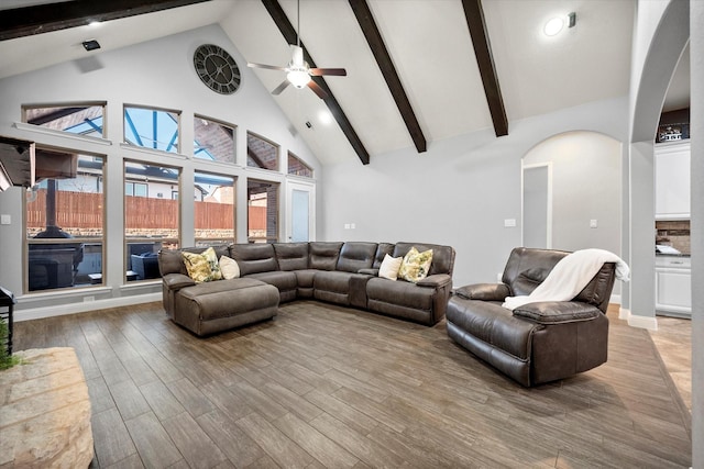 living room featuring arched walkways, beam ceiling, light wood finished floors, ceiling fan, and high vaulted ceiling