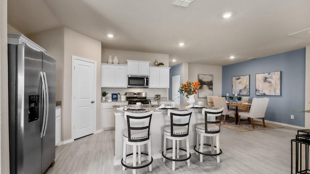 kitchen featuring visible vents, appliances with stainless steel finishes, a kitchen island with sink, white cabinetry, and a kitchen bar