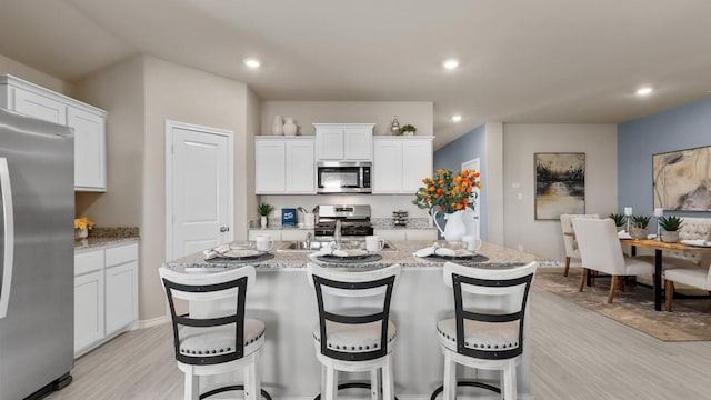 kitchen featuring stainless steel appliances, light wood-style flooring, white cabinets, an island with sink, and a kitchen bar