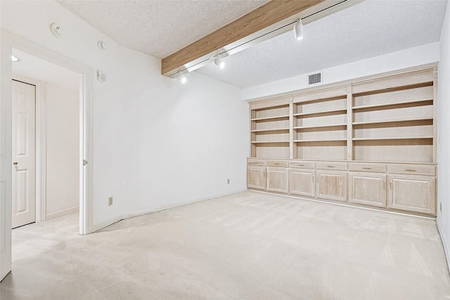 below grade area featuring carpet, visible vents, a textured ceiling, track lighting, and baseboards