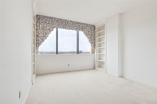 carpeted spare room with built in shelves, a textured ceiling, and baseboards